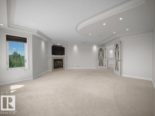 Spacious room featuring a corner fireplace with a stone surround, a large window, and light-colored carpeting - 2423 Tegler Green, Edmonton, AB 