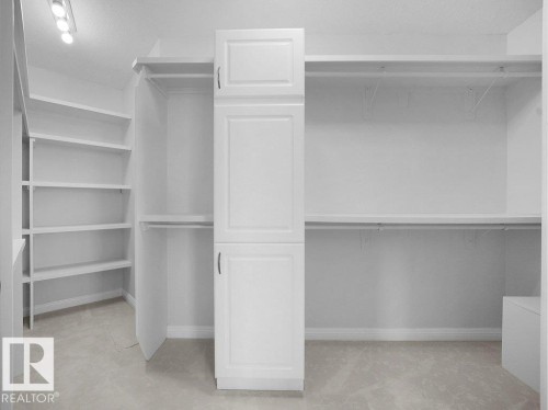 Spacious walk-in closet featuring built-in white cabinetry, extensive shelving, hanging rods, and recessed ceiling lighting - 2423 Tegler Green, Edmonton, AB 