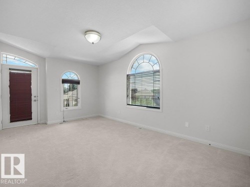 Carpeted room featuring multiple arched windows with blinds, a white door with an arched transom, and a flush-mount ceiling light fixture - 2423 Tegler Green, Edmonton, AB 