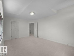 Spacious room featuring neutral carpeting, white walls, and a tray ceiling with a flush-mount light fixture - 
