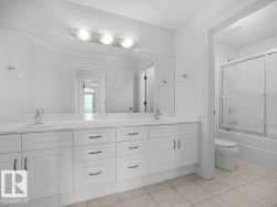 Dual vanity with white cabinetry and integrated sinks, a large mirror, and overhead tri-light fixture - 