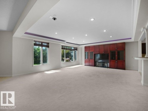 Spacious interior room featuring light-toned carpeting, multiple windows with natural light, and a built-in entertainment unit with rich wood-finish cabinetry - 2423 Tegler Green, Edmonton, AB 