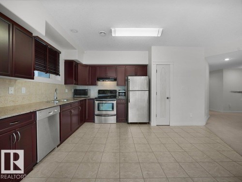 Kitchen featuring dark wood cabinetry, light-toned tiled flooring, light-toned countertop, and stainless steel appliances including a refrigerator, dishwasher, and range - 2423 Tegler Green, Edmonton, AB 