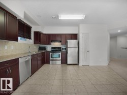 Kitchen featuring dark wood cabinetry, light-toned tiled flooring, light-toned countertop, and stainless steel appliances including a refrigerator, dishwasher, and range - 