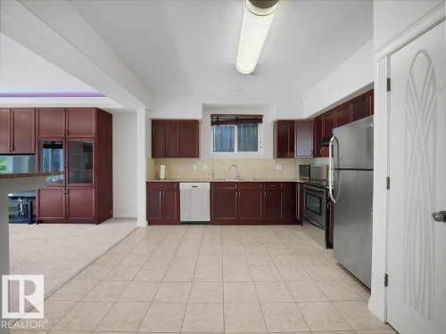 Kitchen featuring wood-finish cabinetry, stainless steel appliances, and tile flooring - 2423 Tegler Green, Edmonton, AB 