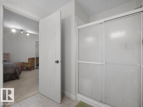 Shower enclosure with textured glass sliding doors, framed by light-toned wall paint and ceramic tile flooring - 2423 Tegler Green, Edmonton, AB 
