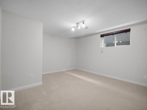 Carpeted room with a textured ceiling, a track light fixture, and a window with blinds - 2423 Tegler Green, Edmonton, AB 