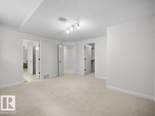 Spacious room featuring light-toned carpet flooring, white walls, and track lighting - 2423 Tegler Green, Edmonton, AB 