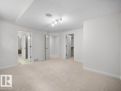 Spacious room featuring light-toned carpet flooring, white walls, and track lighting - 