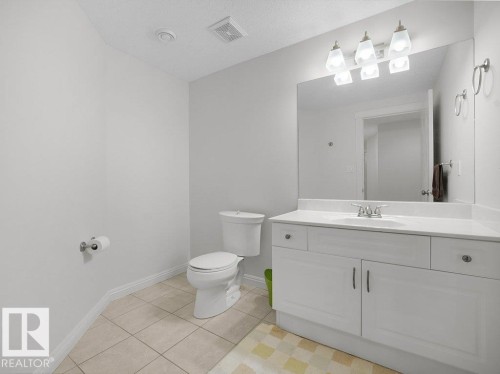 Bathroom featuring a white vanity with integrated sink, a large wall-mounted mirror, brushed nickel light fixture, and tile flooring - 2423 Tegler Green, Edmonton, AB 