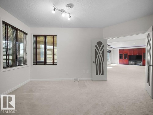 Bright interior space with light-colored carpeting, multiple windows featuring dark wood-finish blinds, and a contemporary track lighting fixture - 2423 Tegler Green, Edmonton, AB 