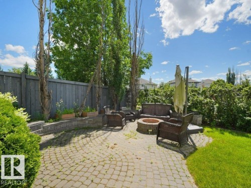 Outdoor patio with paver stone surface, built-in stone fire pit, wood privacy fence, and mature perimeter landscaping - 2423 Tegler Green, Edmonton, AB 