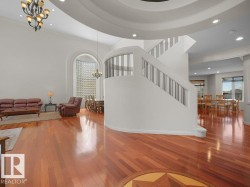 Grand foyer featuring rich wood-finish flooring with an inlaid star design, a curved staircase with metal balusters, and a high ceiling with recessed lighting and a decorative chandelier - 