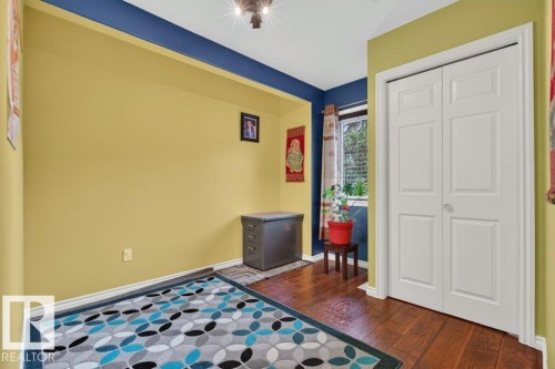 Room featuring wood-finish flooring, white baseboards, a window with blinds, and white bi-fold doors - 11330 101 Street, Edmonton, AB 