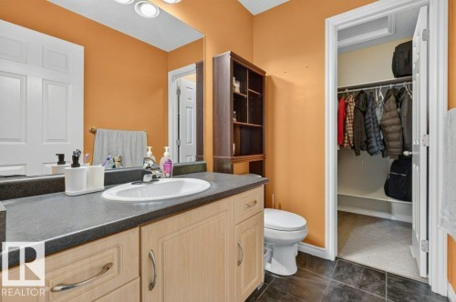 Full bathroom featuring a single vanity with light wood-finish cabinetry, a dark countertop, and an integrated white sink - 11330 101 Street, Edmonton, AB 