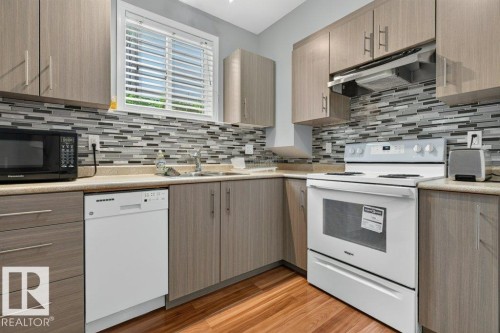 Kitchen featuring light wood-finish cabinetry, a mosaic tile backsplash, composite countertops, and wood-finish flooring - 11330 101 Street, Edmonton, AB 