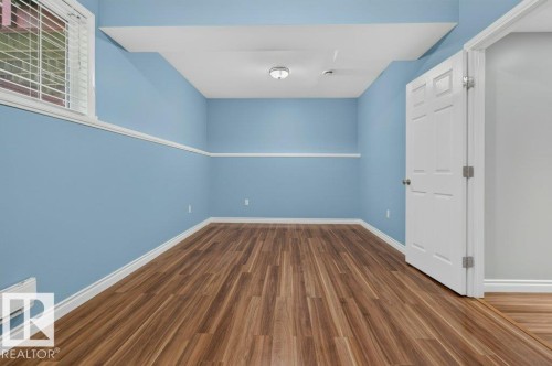 Spacious room featuring wood-finish flooring, light blue walls with a white chair rail, and white trim - 11330 101 Street, Edmonton, AB 