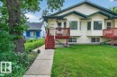 Cream-colored vinyl siding exterior featuring twin bay windows, two red-stained wood decks with railings, and a concrete walkway - 11330 101 Street, Edmonton, AB 