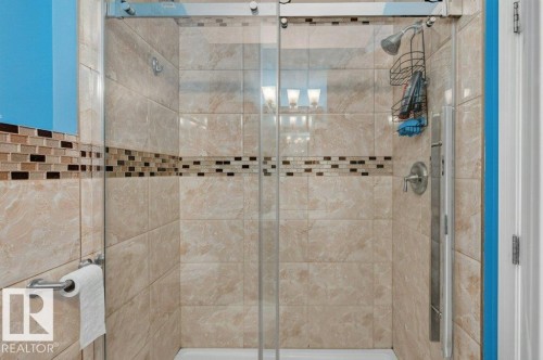 Enclosed shower featuring stone-look tile walls, a mosaic accent band, brushed nickel fixtures, and a clear glass sliding door - 11330 101 Street, Edmonton, AB 