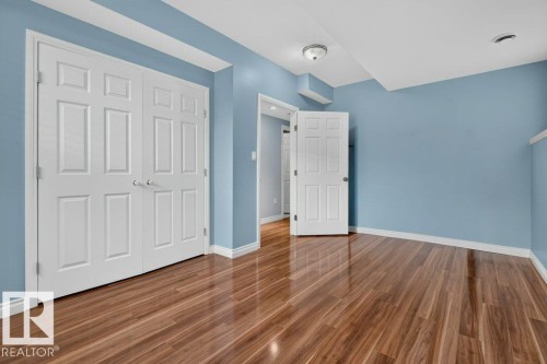 Spacious room featuring wood-finish flooring, white baseboards, and light blue walls - 11330 101 Street, Edmonton, AB 