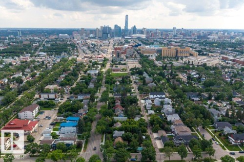Aerial perspective showcasing a sprawling urban landscape with extensive tree-lined streets, a distant city skyline featuring multiple high-rise buildings, and a mix of residential and commercial structures - 11330 101 Street, Edmonton, AB 