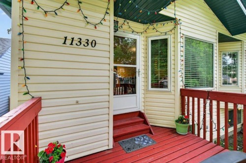 Inviting front entry featuring light-colored siding, a red-painted deck, and a glass-paneled storm door - 11330 101 Street, Edmonton, AB 