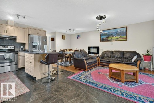 Kitchen featuring light wood-finish cabinetry, stainless steel appliances, and a central island with countertop seating - 11330 101 Street, Edmonton, AB 
