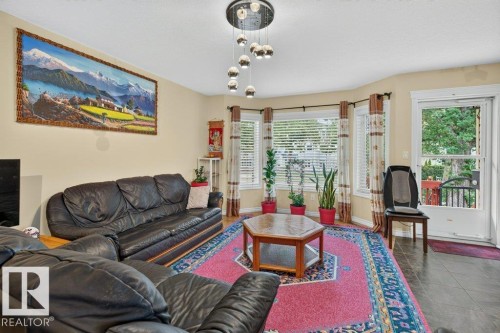 Living room featuring a contemporary multi-bulb chandelier, bay windows with blinds, and durable dark wood-finish flooring - 11330 101 Street, Edmonton, AB 
