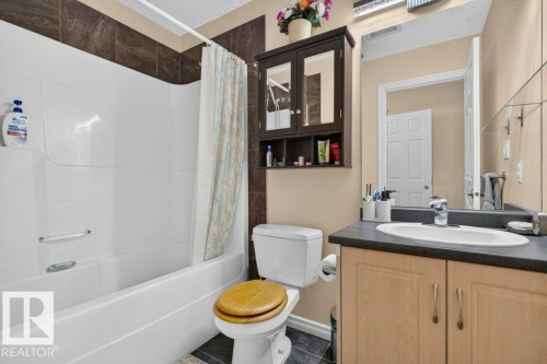 Full bathroom featuring a white tub/shower combination, dark tiled bath surround, and light wood-finish vanity with a dark countertop and integrated sink - 11330 101 Street, Edmonton, AB 