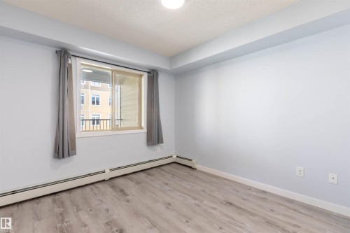 Spacious room featuring wood-finish flooring, a large window with privacy drapes, and light blue walls - 403 25 Element Dr, St. Albert, AB - Indoor Photo Showing Other Room