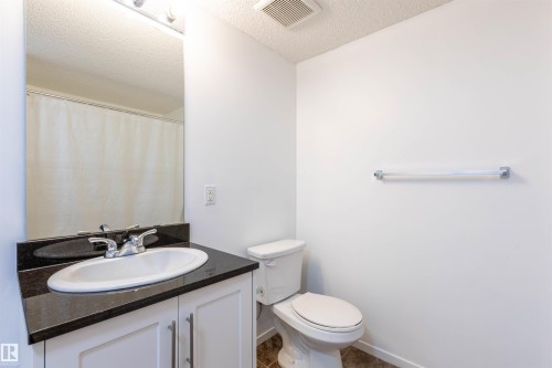 Bathroom featuring a white toilet, chrome towel bar, and a vanity with a dark countertop, integrated sink, and white cabinetry with chrome pulls - 403 25 Element Dr, St. Albert, AB - Indoor Photo Showing Bathroom