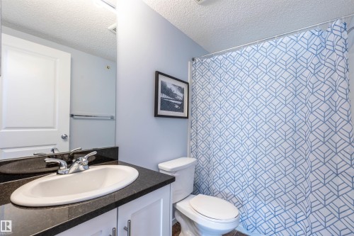 Contemporary bathroom featuring a dark countertop with an undermount sink, a chrome-finish faucet, and white cabinetry - 403 25 Element Dr, St. Albert, AB - Indoor Photo Showing Bathroom