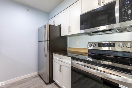 Modern kitchen featuring white shaker cabinetry, dark countertops, and stainless steel appliances including a refrigerator, range, and microwave - 403 25 Element Dr, St. Albert, AB - Indoor Photo Showing Kitchen