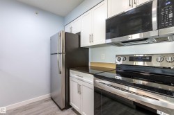 Modern kitchen featuring white shaker cabinetry, dark countertops, and stainless steel appliances including a refrigerator, range, and microwave - 