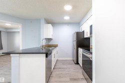 Galley-style kitchen featuring light wood-finish flooring, white cabinetry, dark countertops, a stainless steel sink with a gooseneck faucet, and recessed lighting - 