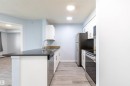 Galley-style kitchen featuring light wood-finish flooring, white cabinetry, dark countertops, a stainless steel sink with a gooseneck faucet, and recessed lighting - 403 25 Element Dr, St. Albert, AB  - Indoor Photo Showing Kitchen With Double Sink 