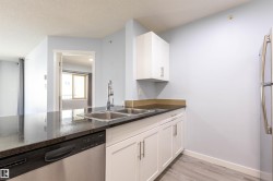 Kitchen featuring stainless steel double basin sink, chrome faucet, black granite-look countertops, white cabinetry with brushed nickel pulls, and a stainless steel dishwasher - 
