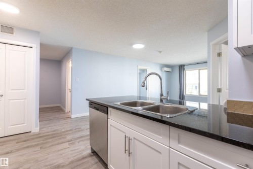 Kitchen island featuring a double basin stainless steel sink with a gooseneck faucet, black stone countertop, and white shaker-style cabinetry - 403 25 Element Dr, St. Albert, AB - Indoor Photo Showing Kitchen With Double Sink