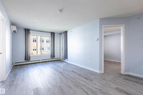 Spacious room featuring wood-finish flooring, light blue walls, and a large window with privacy drapes - 403 25 Element Dr, St. Albert, AB - Indoor Photo Showing Other Room