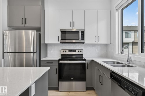 Modern kitchen featuring stainless steel appliances, dual-tone cabinetry, light-toned countertops, a hexagonal tile backsplash, and a double basin sink - 33 11910 35 Avenue, Edmonton, AB 