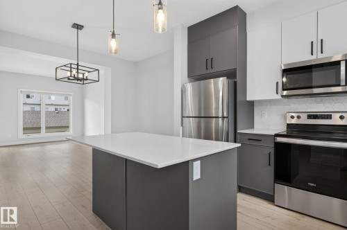 Open-concept kitchen featuring two-tone cabinetry, stainless steel appliances, a white quartz island, and wood-finish flooring - 33 11910 35 Avenue, Edmonton, AB 