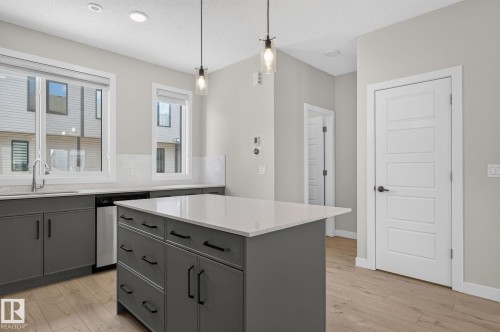 Kitchen featuring a central island with white countertop, grey cabinetry, and wood-finish flooring - 33 11910 35 Avenue, Edmonton, AB 