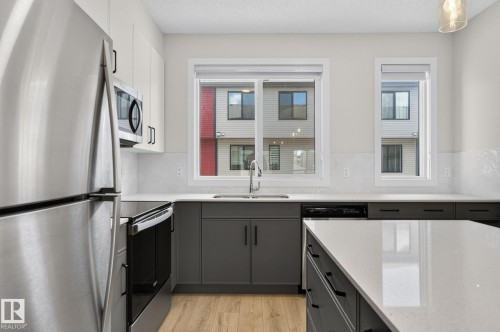 Modern kitchen featuring a stainless steel refrigerator, built-in microwave, and range - 33 11910 35 Avenue, Edmonton, AB 