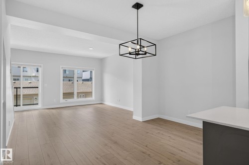 Open-concept living area featuring wood-finish flooring, a contemporary geometric chandelier, and crisp white walls - 33 11910 35 Avenue, Edmonton, AB 