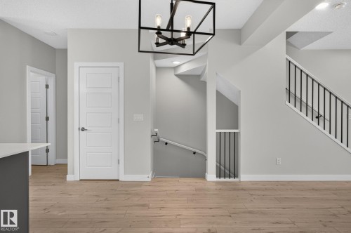 Entryway featuring wood-finish flooring, a contemporary black metal chandelier, and a five-panel interior door - 33 11910 35 Avenue, Edmonton, AB 