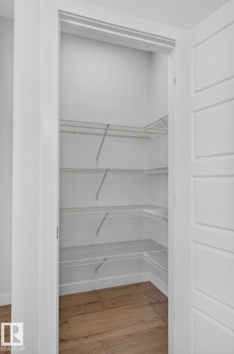 Recessed pantry featuring multiple levels of wire shelving, wood-finish flooring, and crisp white trim - 33 11910 35 Avenue, Edmonton, AB 