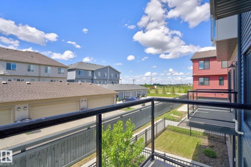 Balcony featuring black metal railings with glass inserts, offering exterior views of residential buildings with varied siding and rooflines, a fenced yard area, and distant open green spaces - 33 11910 35 Avenue, Edmonton, AB 