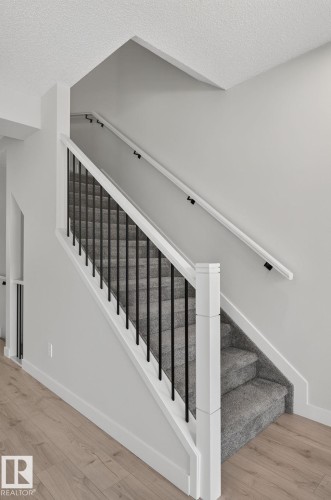 Modern staircase featuring black metal balusters, white handrails, and gray carpeted treads - 33 11910 35 Avenue, Edmonton, AB 