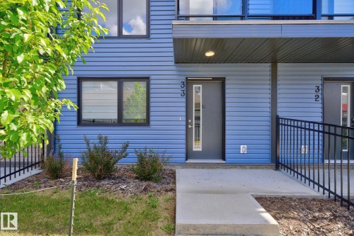 Blue horizontal siding exterior with black window frames, a gray front door featuring a vertical glass insert, and a concrete walkway - #33 11910 35 Av Sw, Edmonton, AB - Outdoor With Exterior