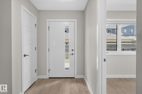 Entryway featuring wood-finish flooring, a modern white door with frosted glass paneling, and a contemporary panel-style interior door - 33 11910 35 Avenue, Edmonton, AB 